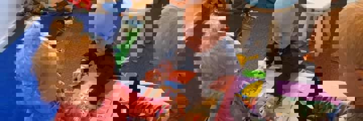 To små børn i alderen 1 til 2 år laver puslespil, mens et tredje barn kigger på.