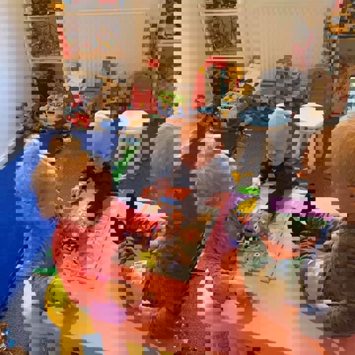 To små børn i alderen 1 til 2 år laver puslespil, mens et tredje barn kigger på.