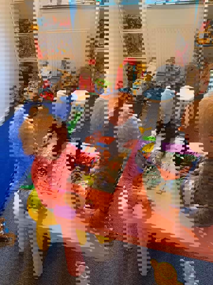 To små børn i alderen 1 til 2 år laver puslespil, mens et tredje barn kigger på.